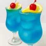 Two blue curacao cocktails with lemon and cherry garnish
