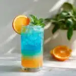A tall clear glass of Blue Citrus Cooler with visible ombre layers
