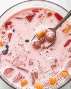 Spoon scooping fruit from a pink punch bowl filled with vibrant fruit chunks
