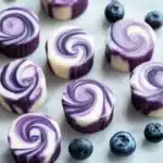 Blueberry swirl yogurt bites stacked on a white plate with blueberries