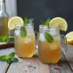 A refreshing glass of iced herbal nettle tea with herbs in the background