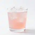 A glass of homemade rhubarb soda garnished with fresh rhubarb and ice.