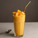 Delicious mango smoothie without banana in a glass topped with fresh mango slices.