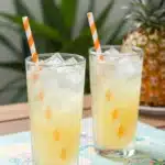 Refreshing Pineapple Lemonade Soft Glow in a glass with tropical fruits.