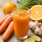 Bright orange Carrot Ginger Juice in a glass, garnished with fresh ginger and carrots.