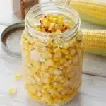 A jar of pickled corn with spices and fresh herbs ready to serve.